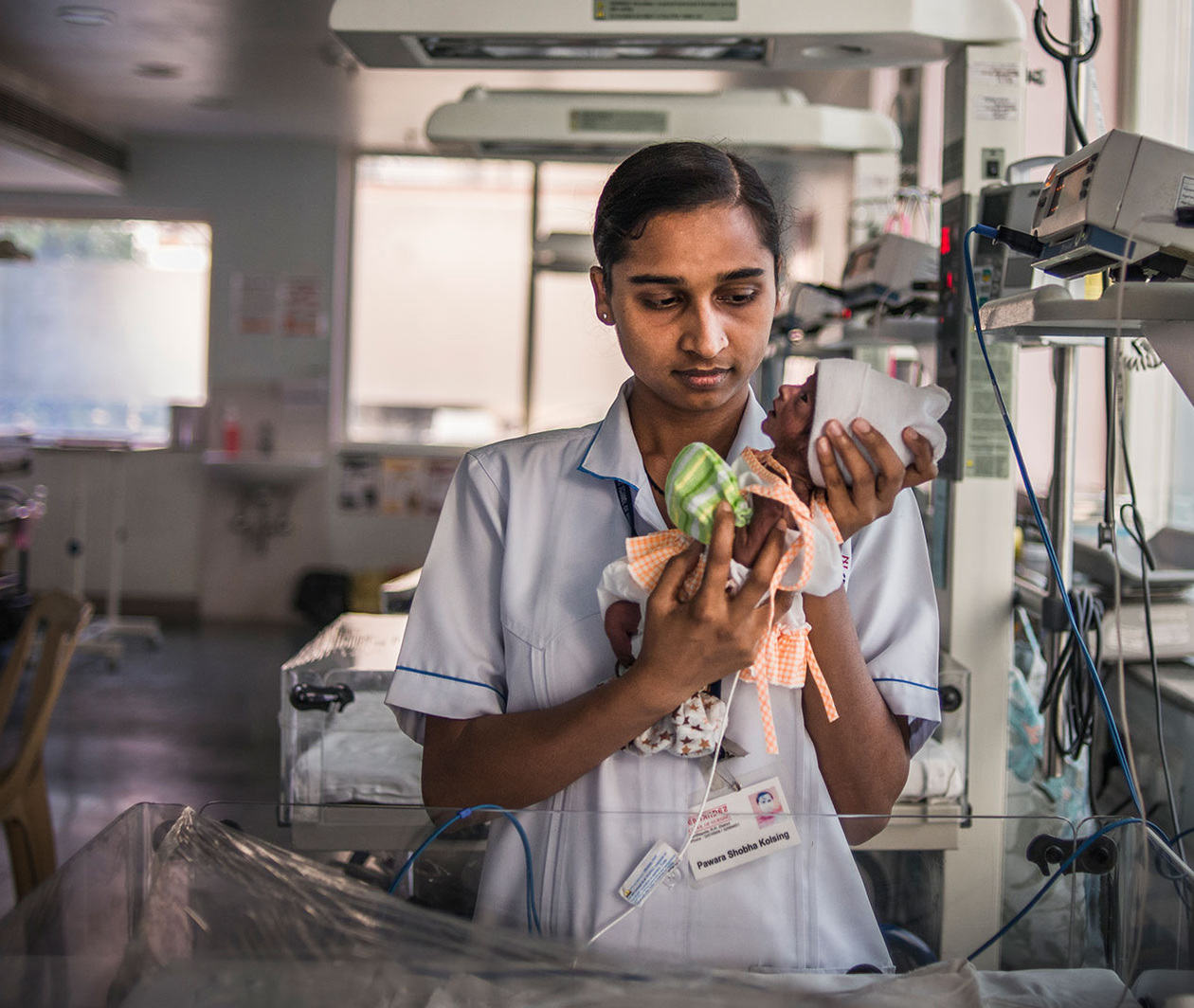 Nurse holding a very preterm baby in a neonatal intensive care unit, India