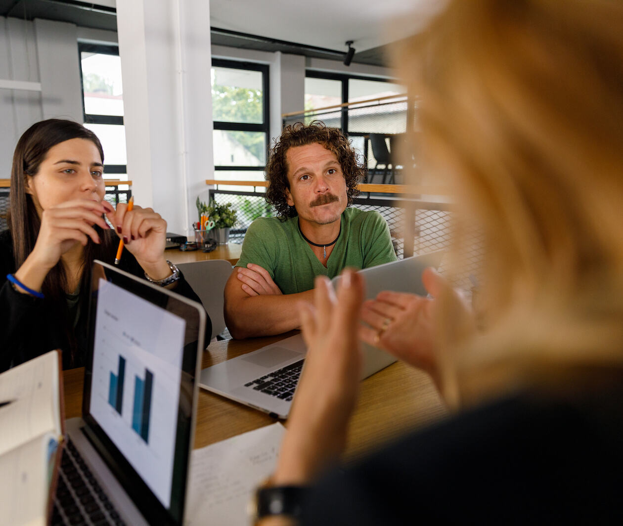 Over the shoulder view of businesswoman interviewing two java developers, which a laptop with charts on it