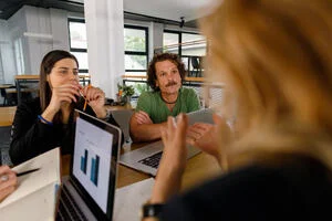 Over the shoulder view of businesswoman interviewing two java developers, which a laptop with charts on it