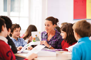 A teacher shows a colourful card to a group of young children around her