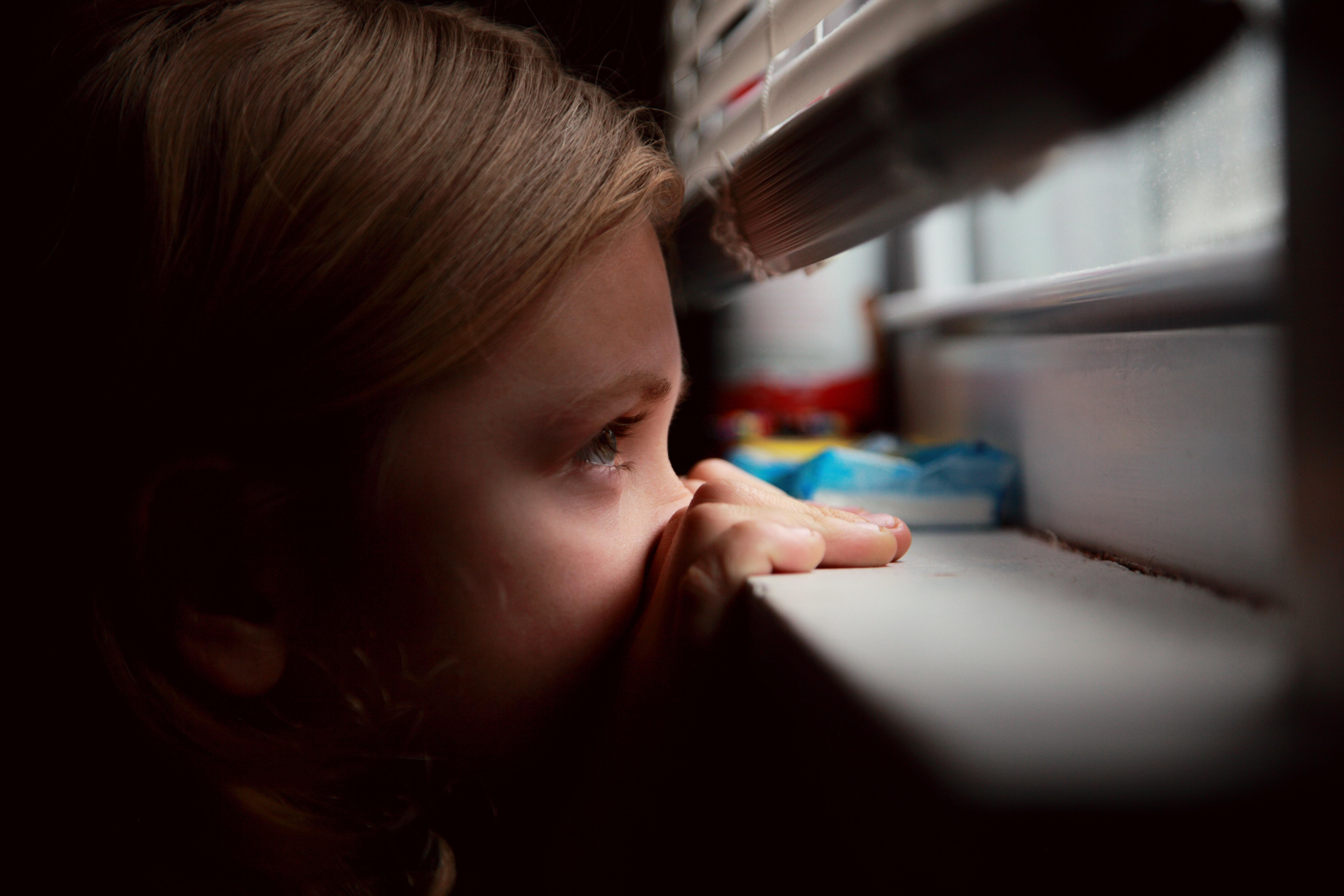 Young girl peering out of a window