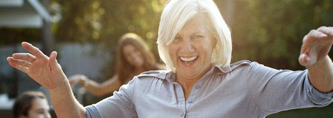 A playful image of an older woman, a teenager and young girl having fun hula hooping in a back garden next to a swimming pool.