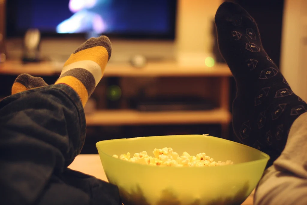 Image of children's legs resting on a lounge next to a bowl of popcorm in front of a television