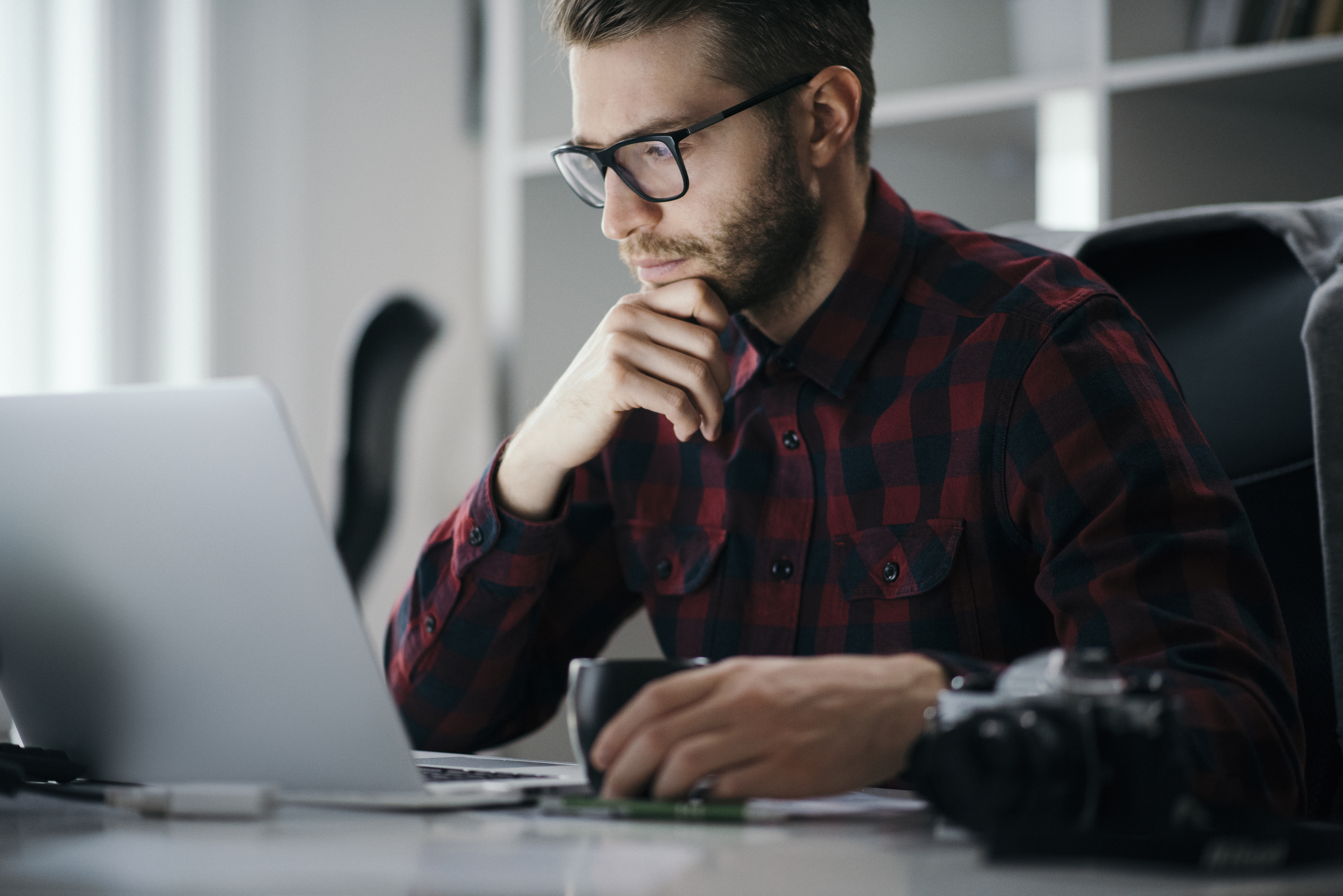 A person looking at their laptop whilst holding a cup of coffee.