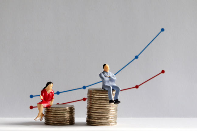image of figure of a man and a figure of a woman both sat on a pile of coins. The coin pile the man is sat on is much higher.