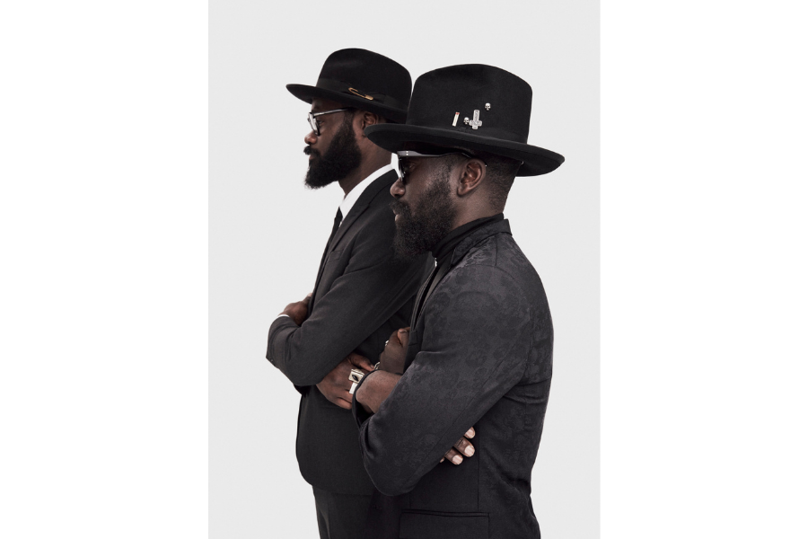 A profile view of Sam and Shaka of ACF, both suited and wearing hats.