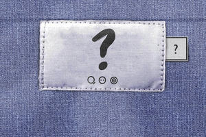 Clothing label bearing a question mark, three wash symbols with the text 'be curious', 'find out', and 'do something'. A Fashion Revolution tab appears to the right of the main label.