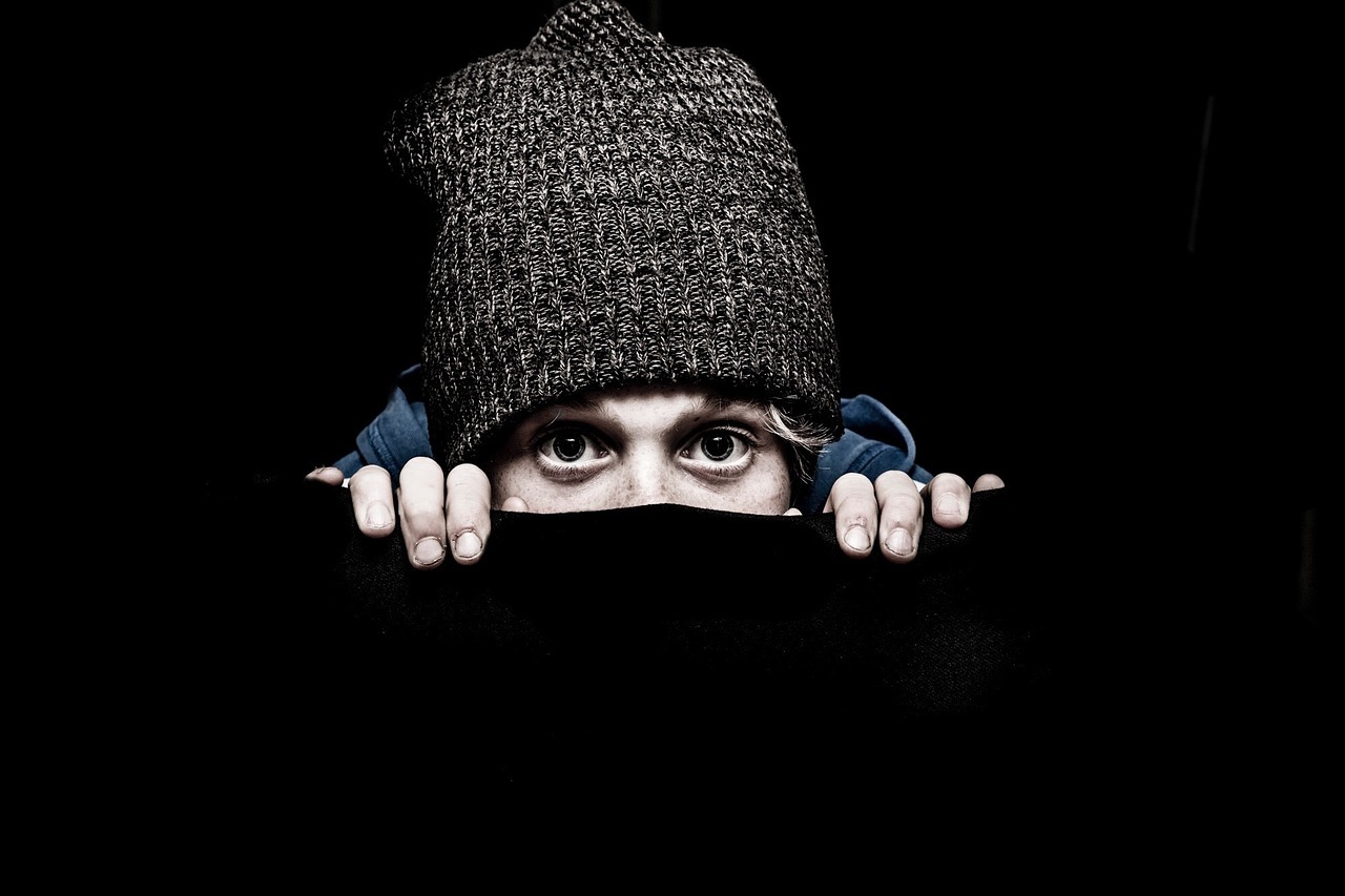 A young man in a woollen hat peeps shyly over a wall.