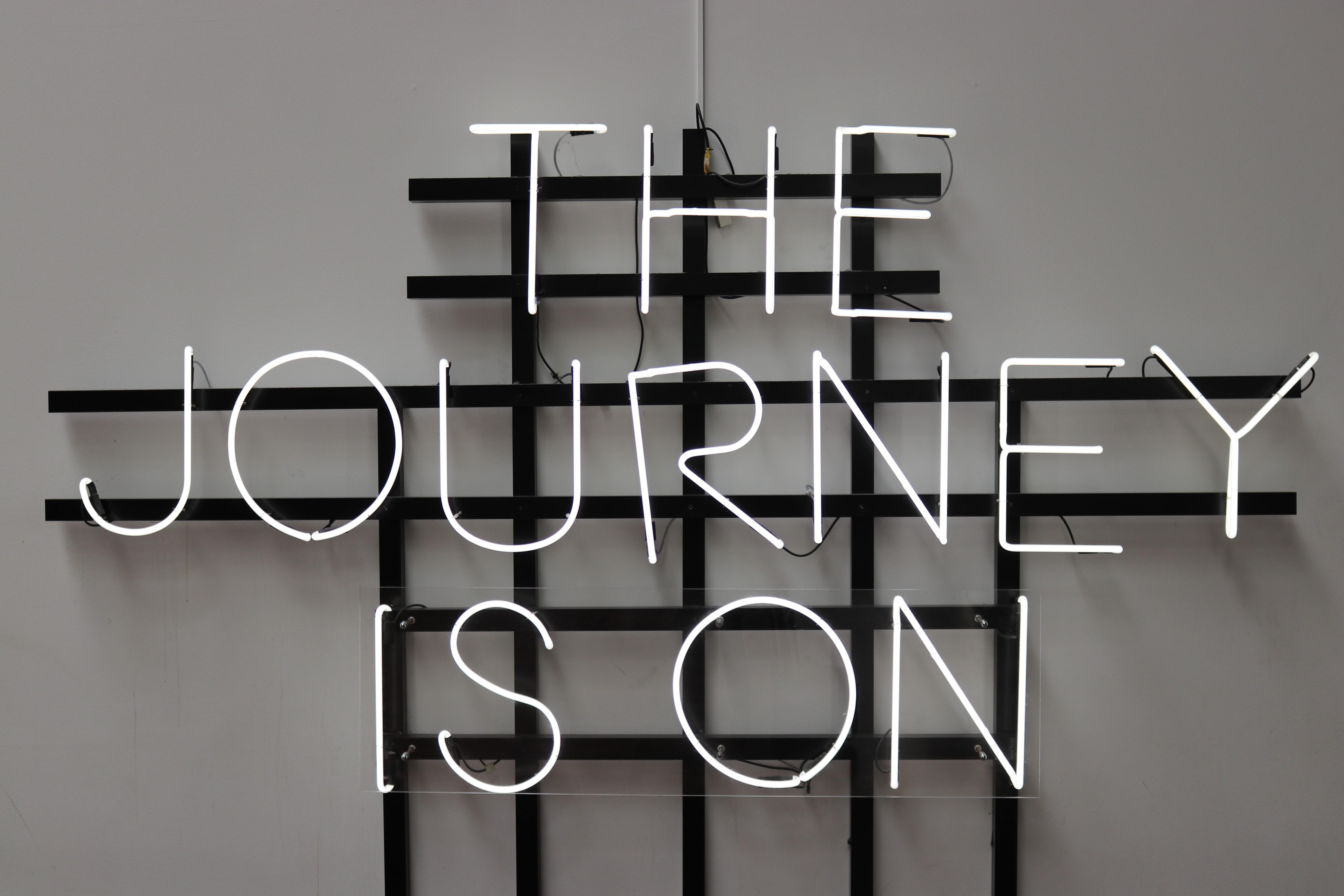 White writing on black hatched background led sign - the journey is on