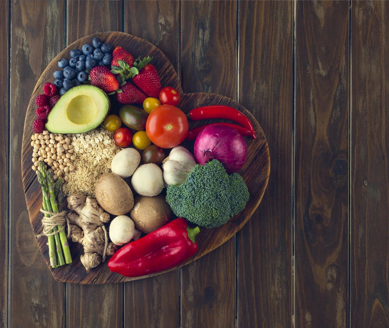 Healthy food with fruit, vegetables, grains and high fibre foods on a heart shape cutting board in a rustic wood textures background. These are the food that provide nutritions to prevent age-related disease such as chronic conditions.