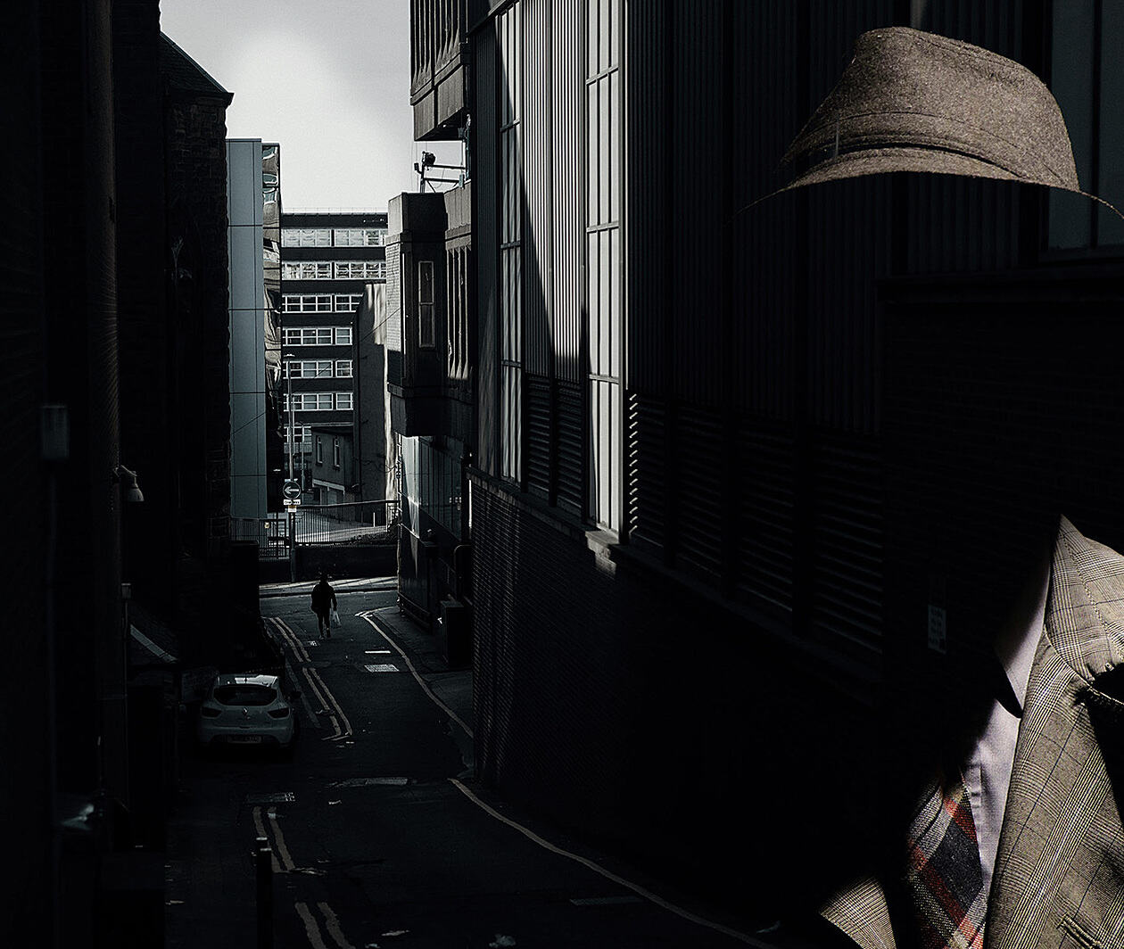 A dark city alleyway overlaid by the shadowy figure of a faceless detective