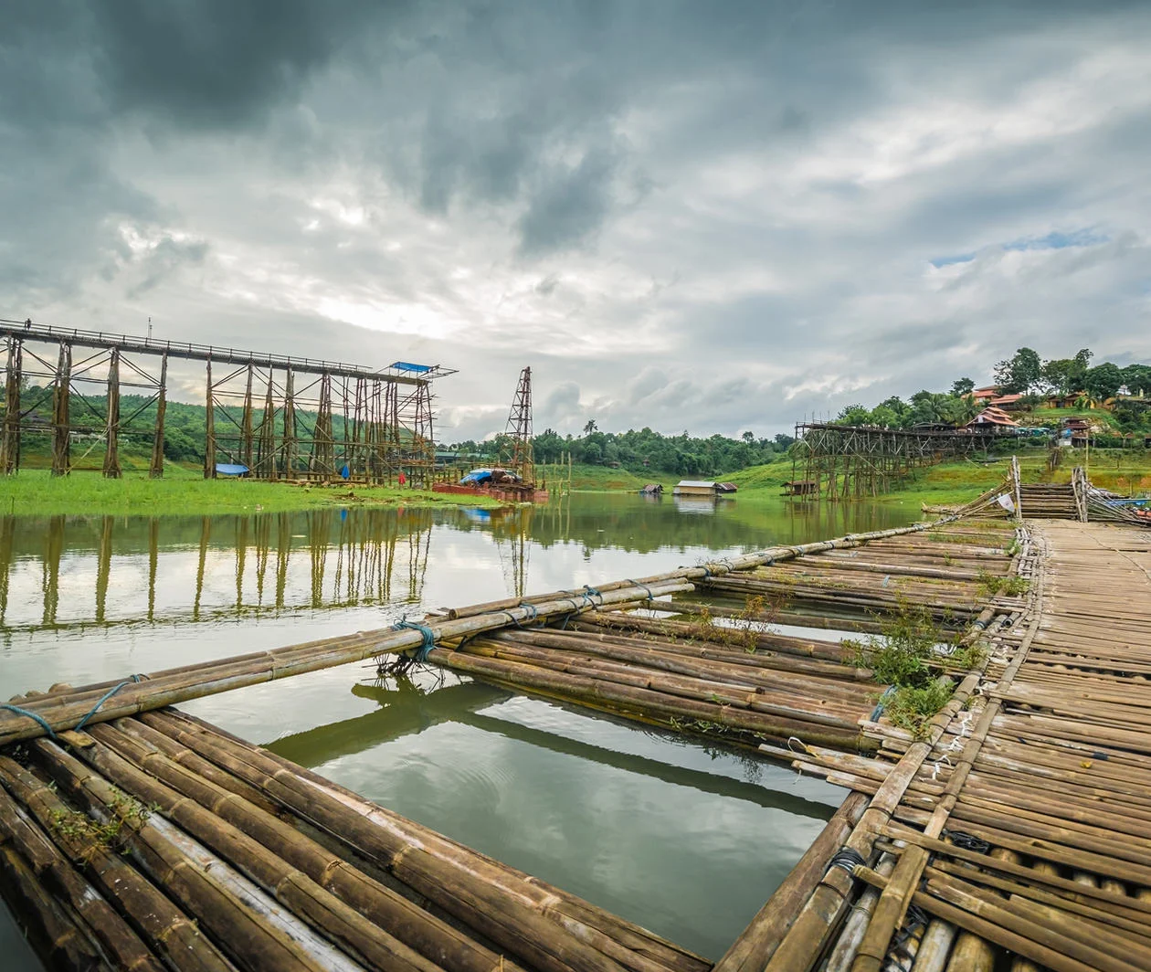 A rural bridge in Thailand, mid-construction over water with bamboo dock in foreground