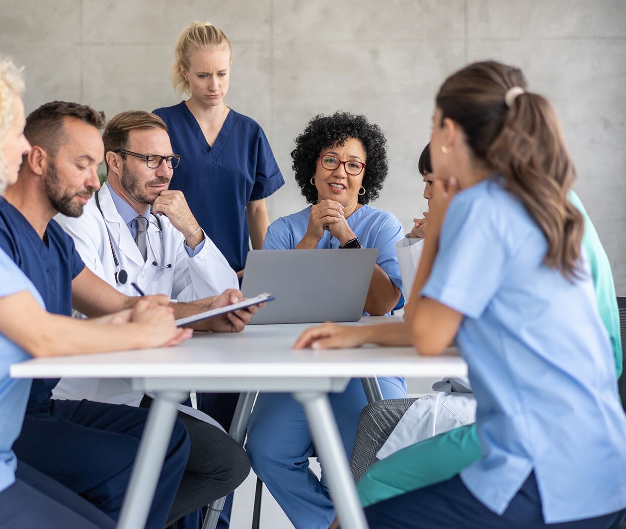 A diverse team of healthcare professionals collaborate around a laptop in a meeting room