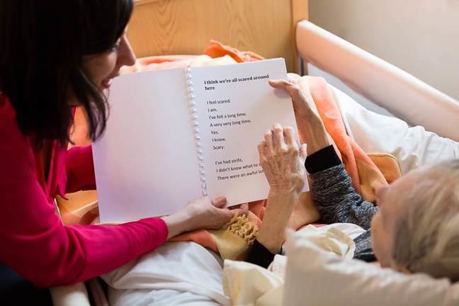 Image of two people in a care home looking at a piece of text in a booklet together