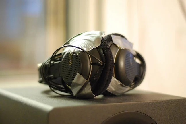 A pair of black headphones mended with ducked tape, placed on a black speaker.