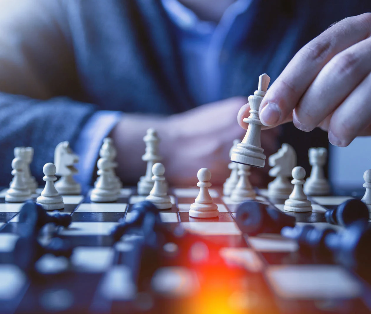 The hands of a man are playing chess. Opponent is unseen. Pieces are knocked down on the board.