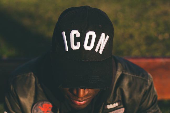 A close-up of a man in a baseball cap displaying the word 'Icon'.