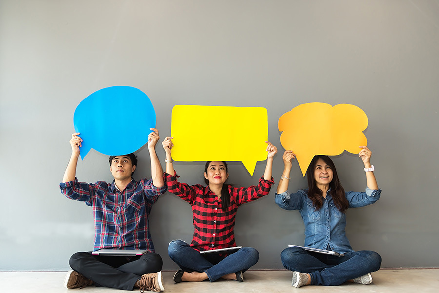 Adult asian man and two women holding coloured paper speech bubbles above their heads.