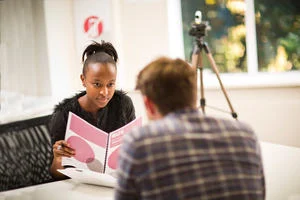 Man and woman sit across from each other and conduct a recorded speaking test