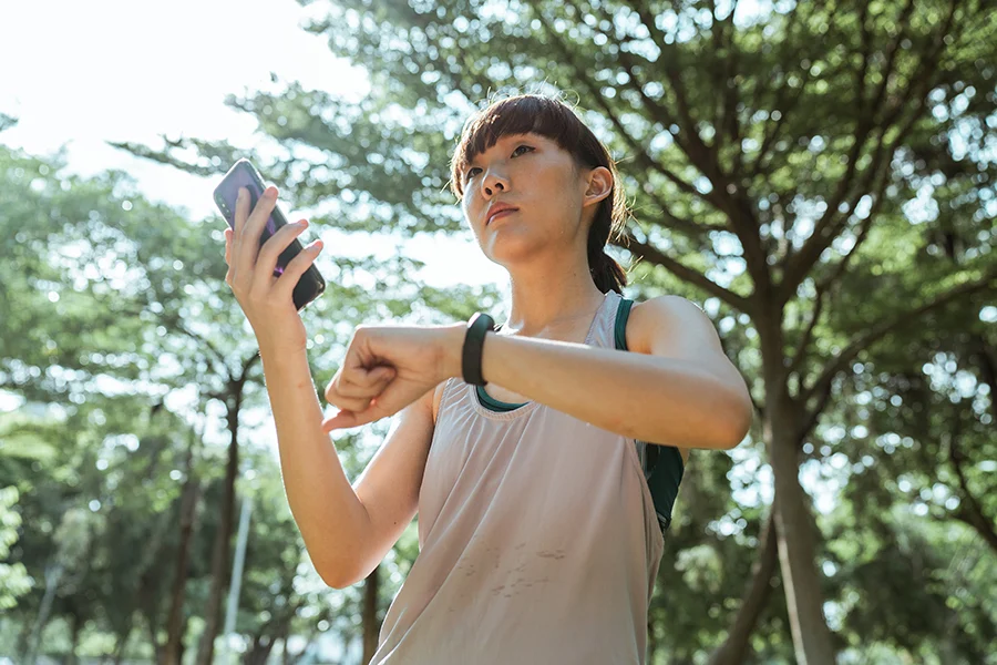 Fit woman outdoors looking at phone and watch