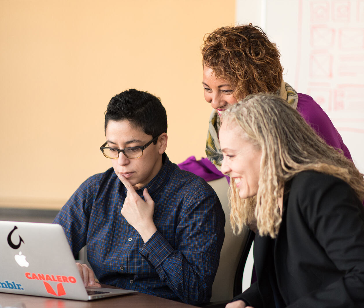 3 female designers looking at a computer with smile, thinking about how to select health building material for healthier community.