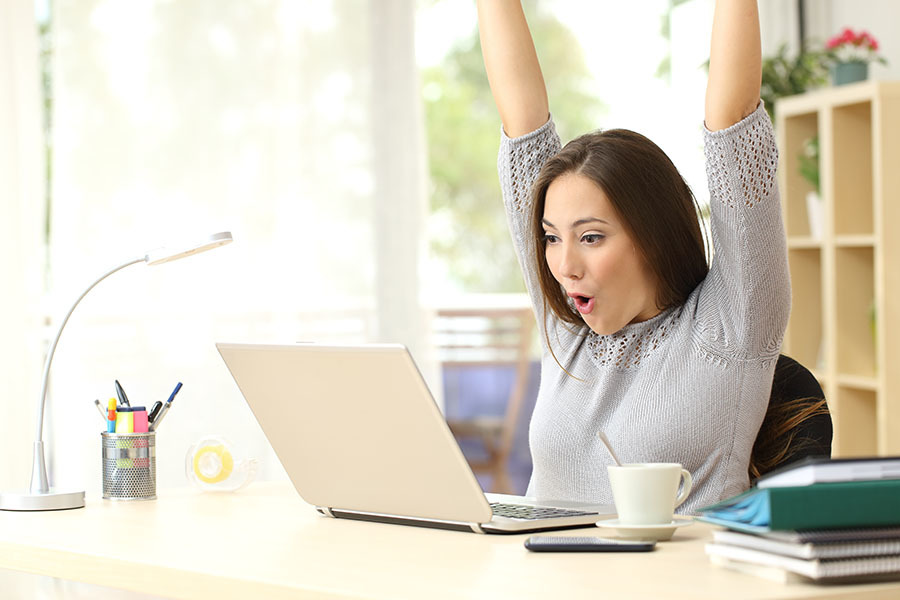 Woman behind her laptop cheering with her hands in the air