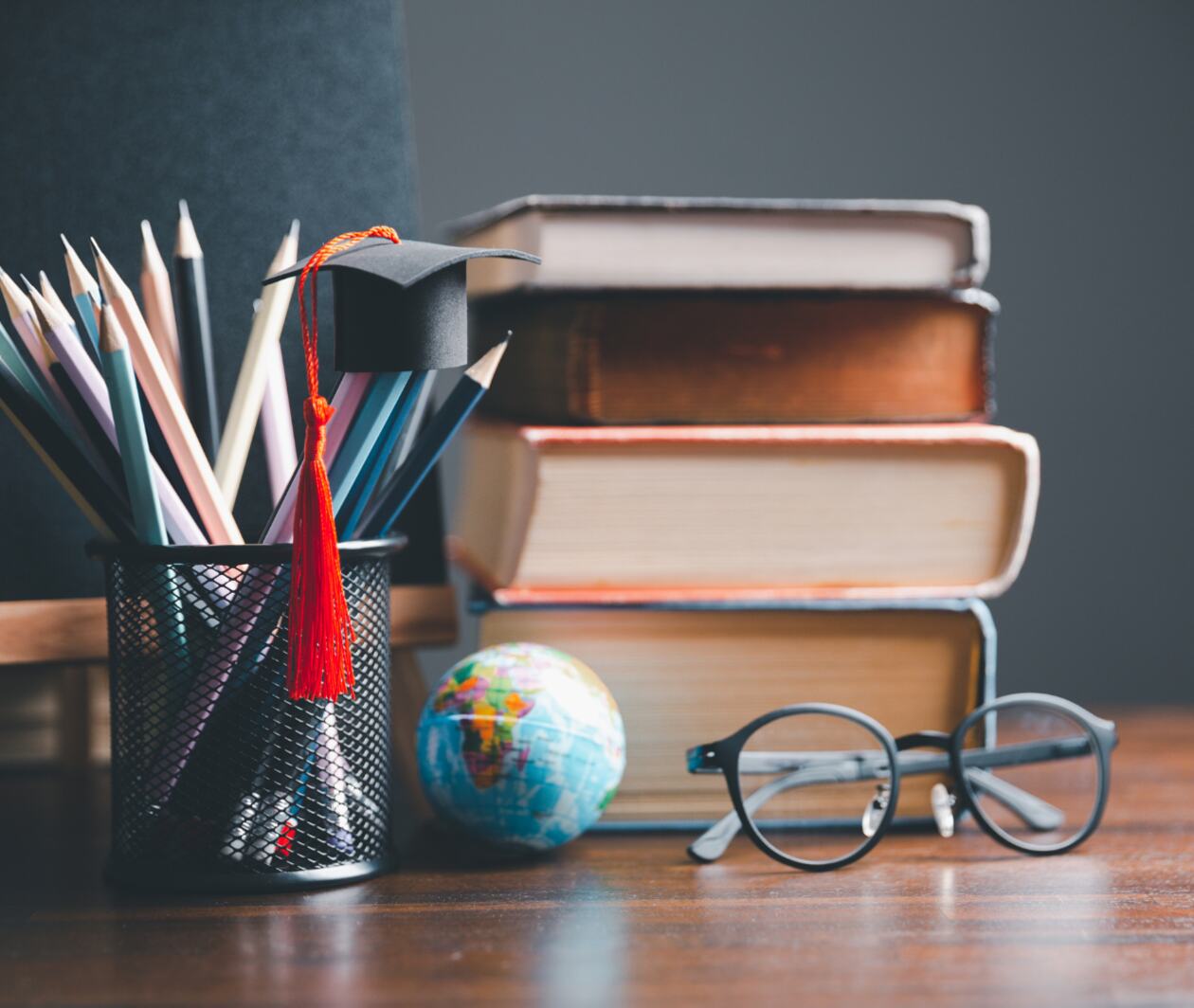 A pen holder, a bachelor's hat hanging on a pencil, four books, a globe model and a pair of glasses next to it.