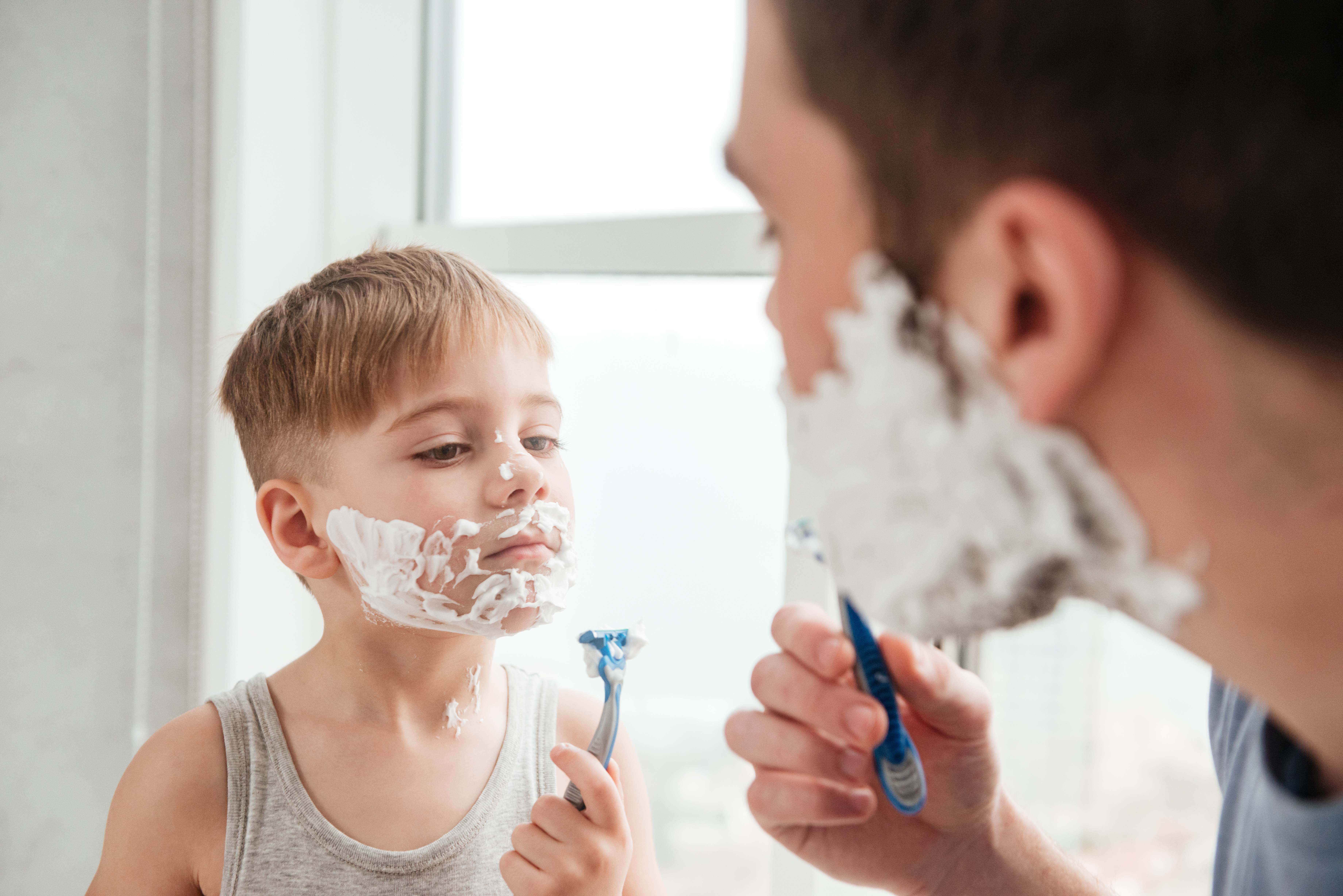 Photo of a man and kid shaving in front of each other. Child seems to imitate his father.