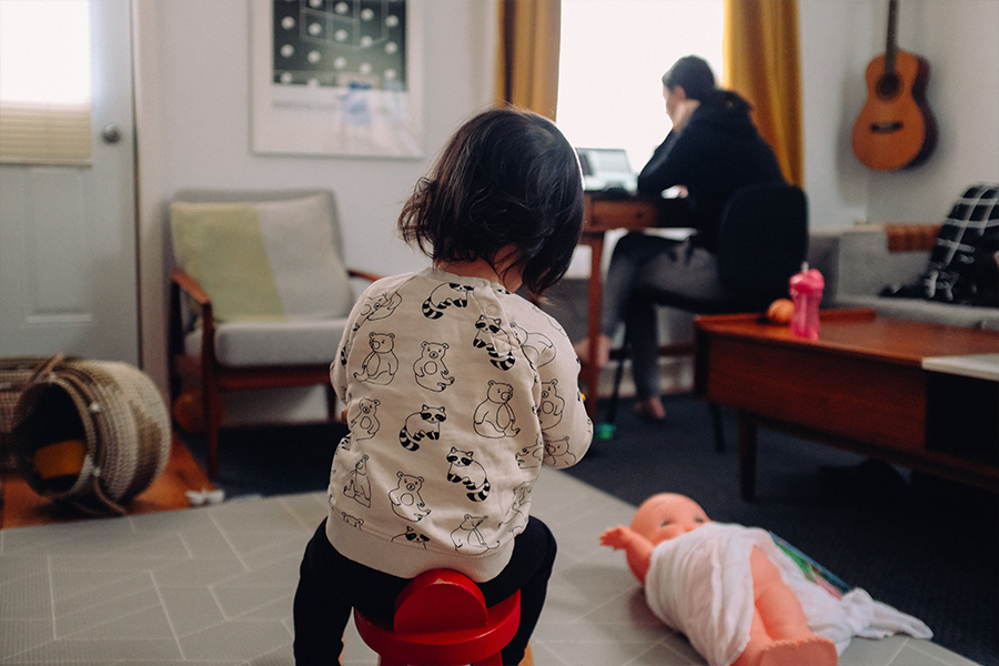 Young girl playing alone while mother is using laptop