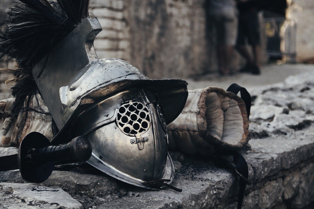 A gladiator helmet lies on some old, grey, stone steps, with its sword lying unused next to it.