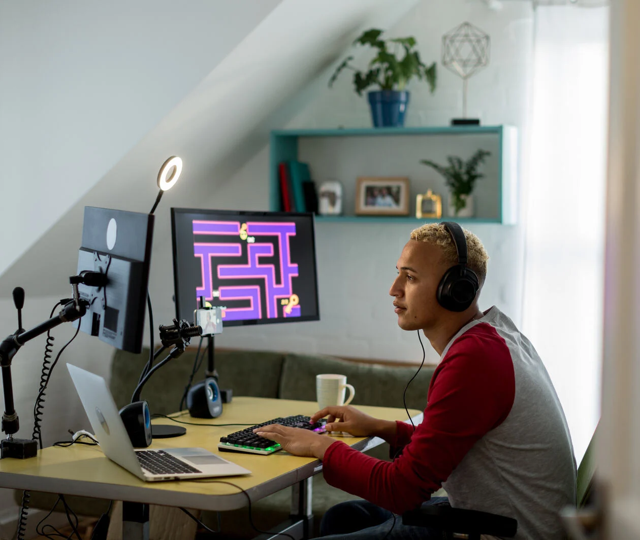 Young man wearing a headset sitting at his desk and playing a game on one of two computer screens.