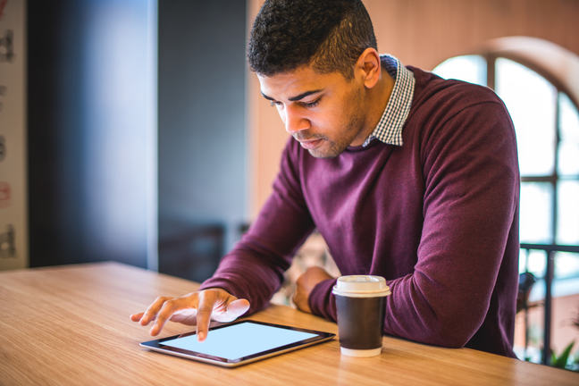 A man sitting at a table with a coffee cup, using his digital tablet.