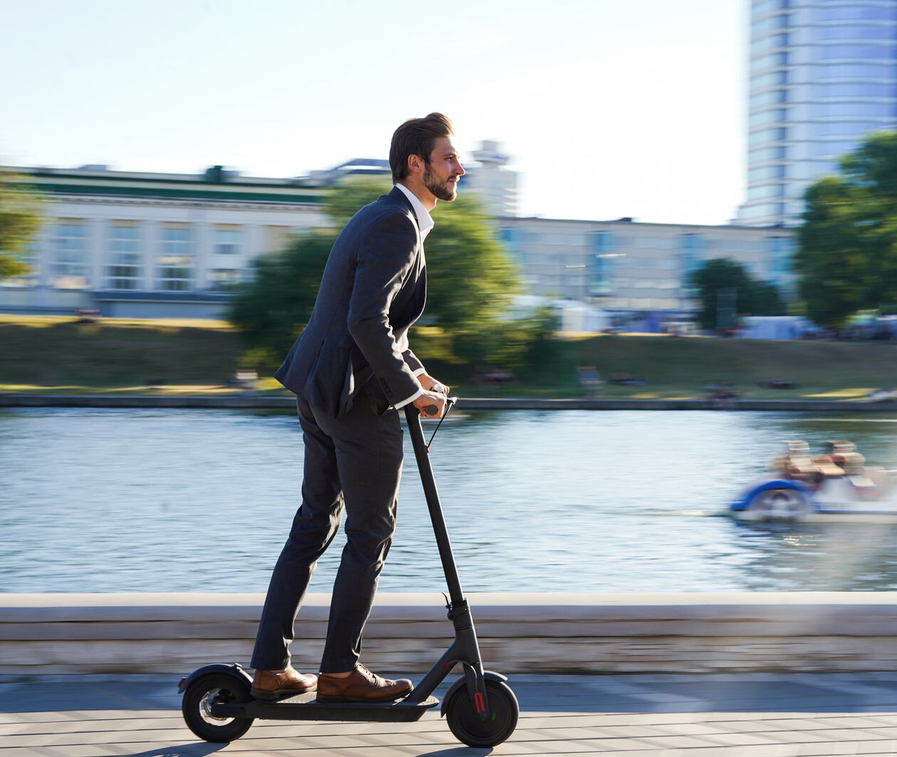 Man in business suit riding scooter along river