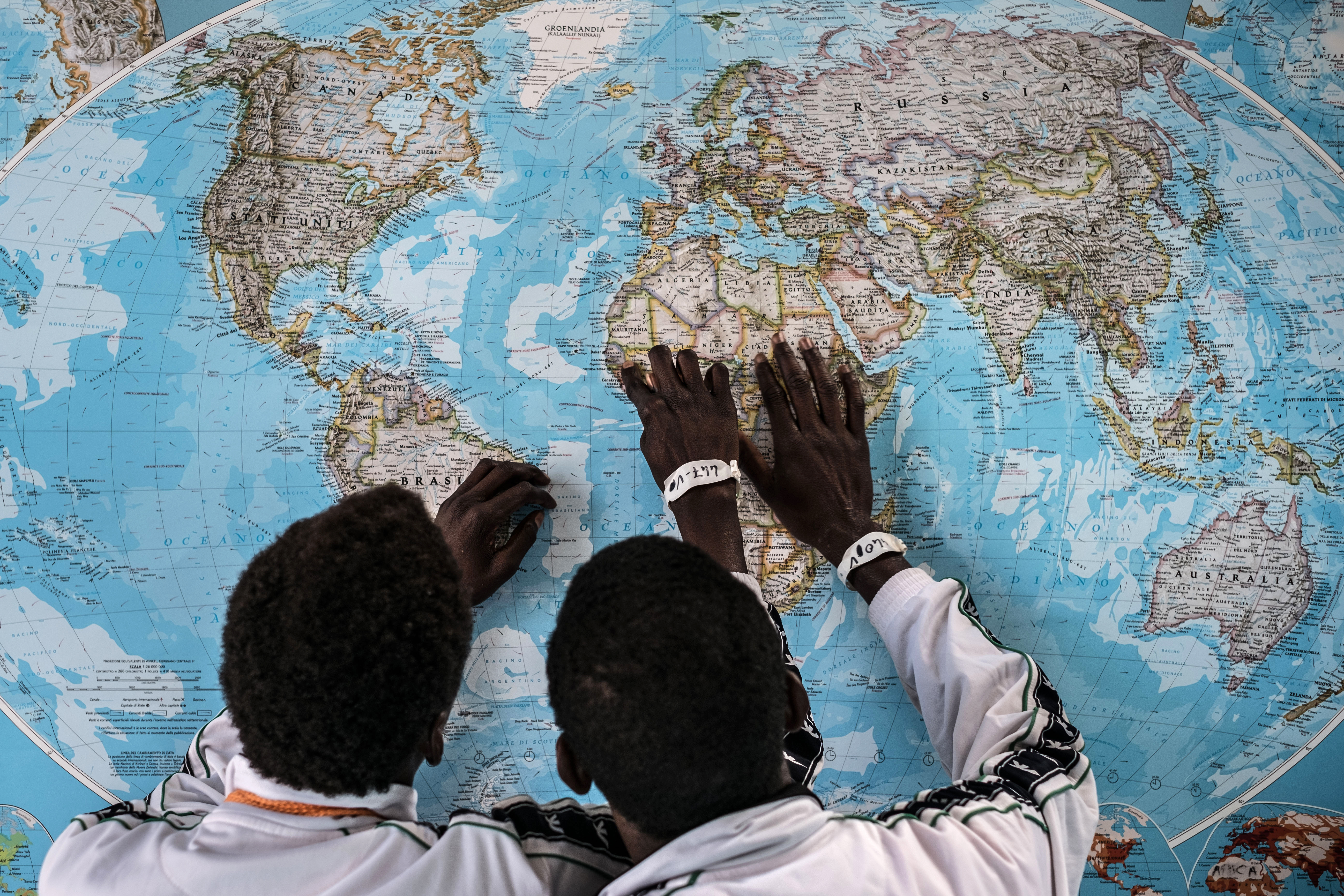 Two teenage boys from Gambia are looking at a map of the world. We see them from behind with their hands on the picture of Africa.