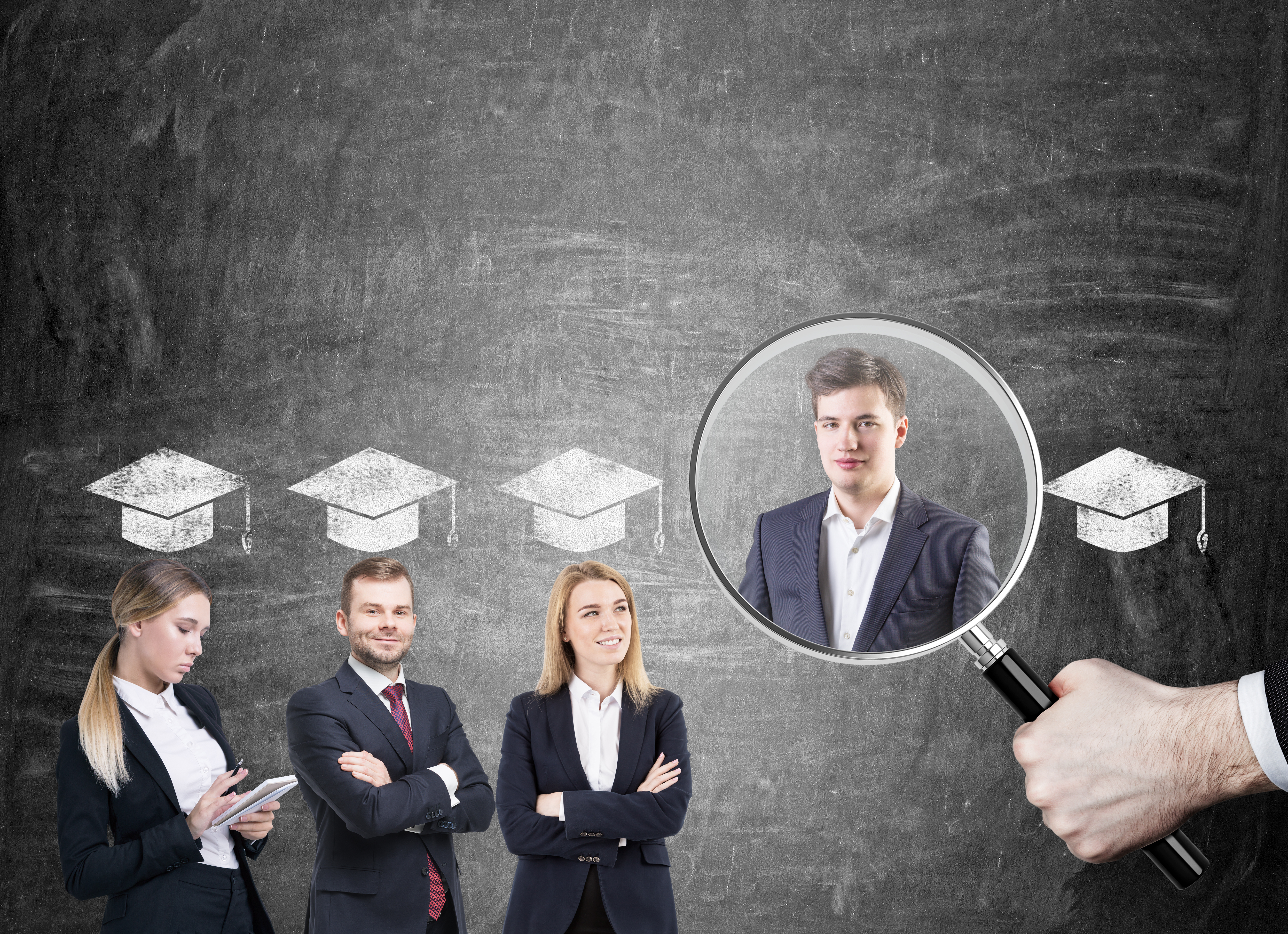 College graduates in suits are standing near a blackboard with graduation hats above their head. A large magnifying glass is hovering above.