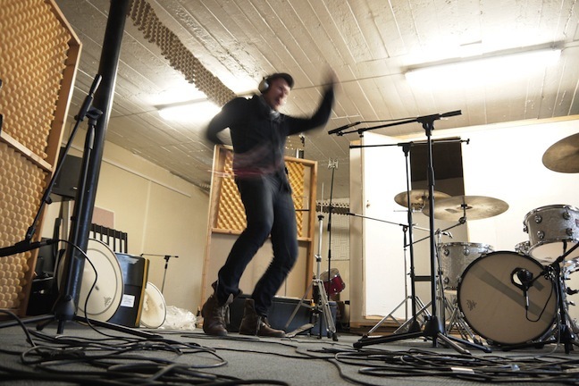 Man standing in a rehearsal roomm playing a tambourine in a fast motion.