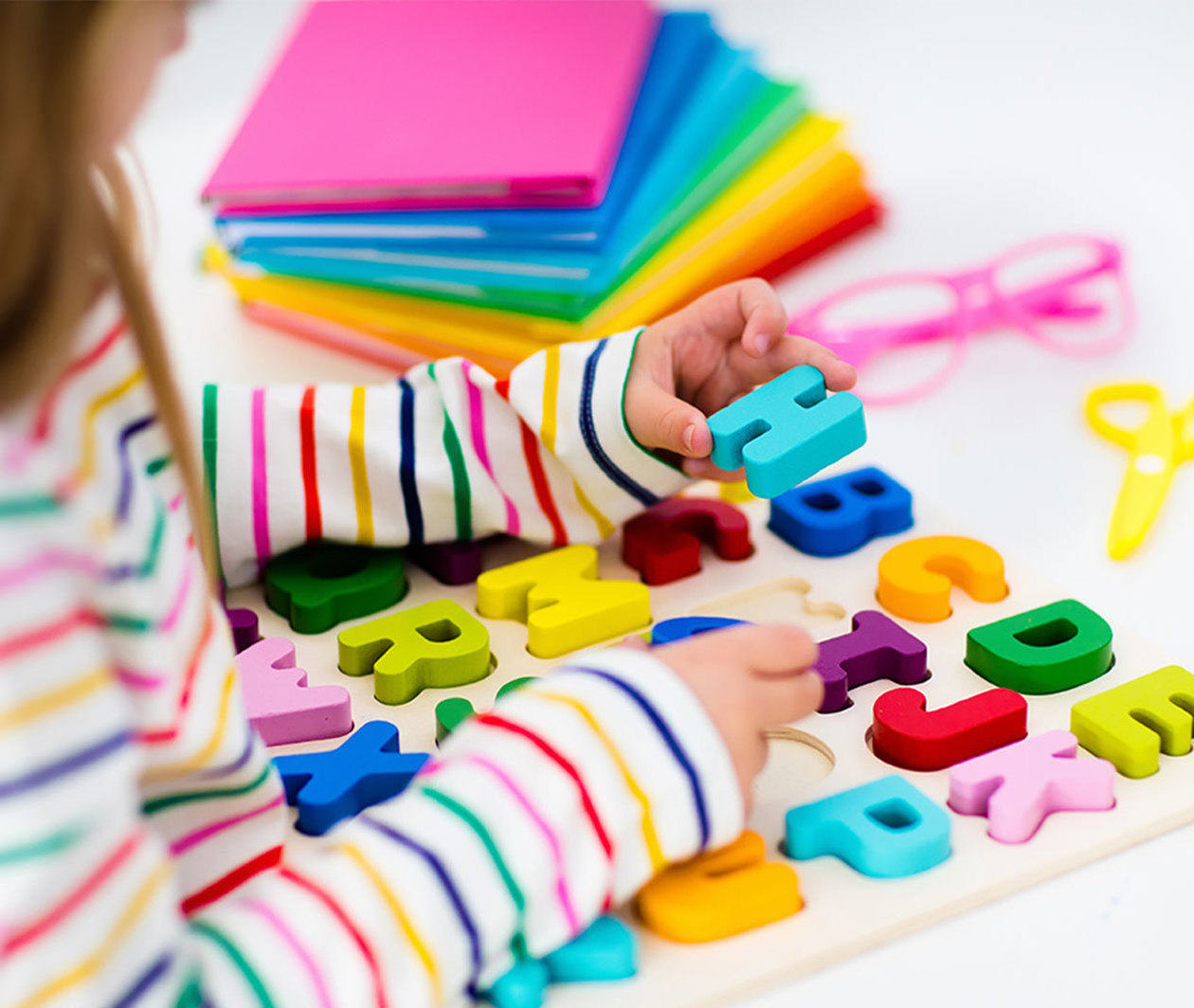 Young girl picking up a blue letter H from a coloured alphabet puzzle.