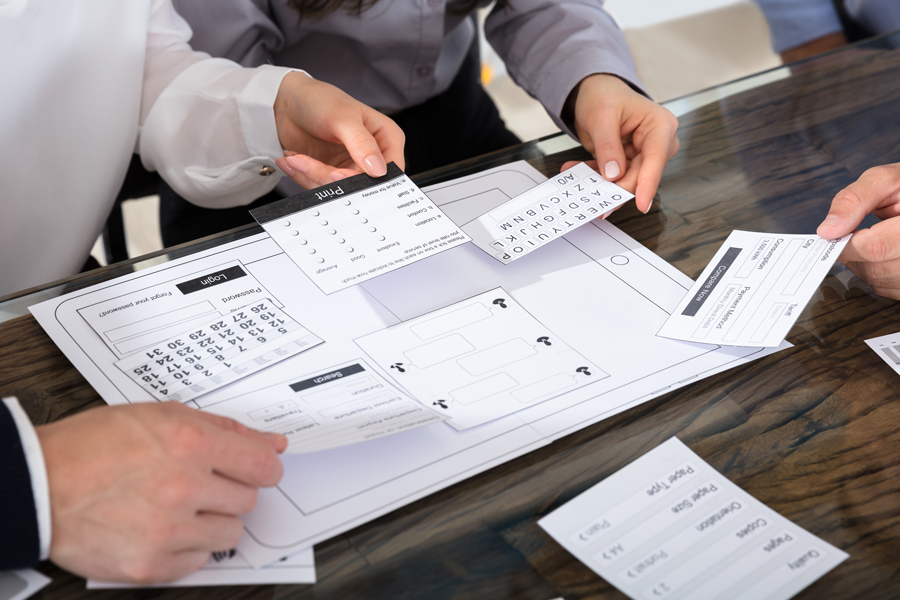 A paper mock-up of a digital device with people placing paper features onto it.