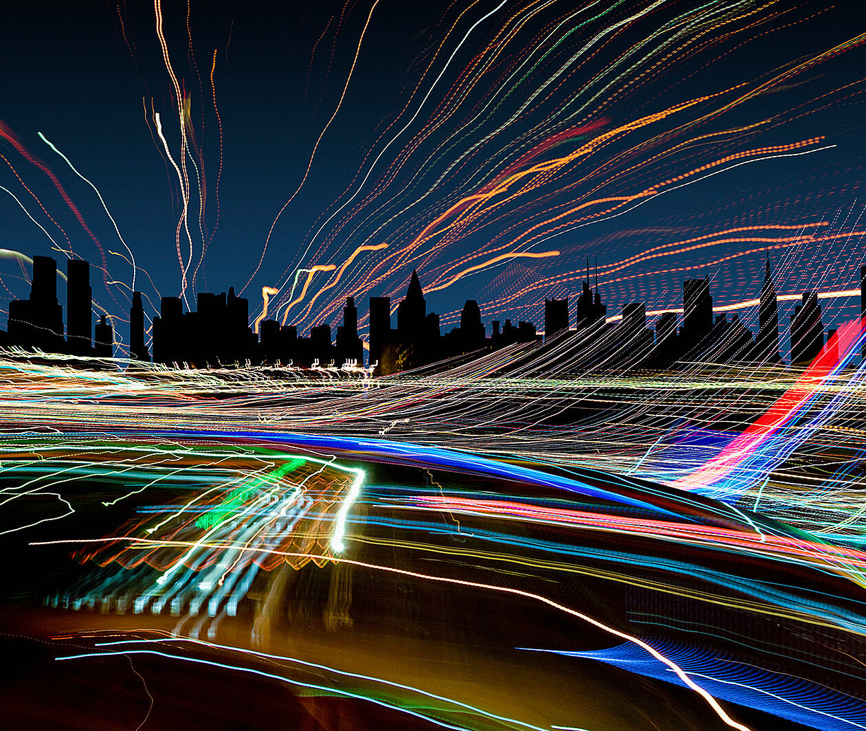 A darkened city skyline with many coloured lines crossing in all directions 