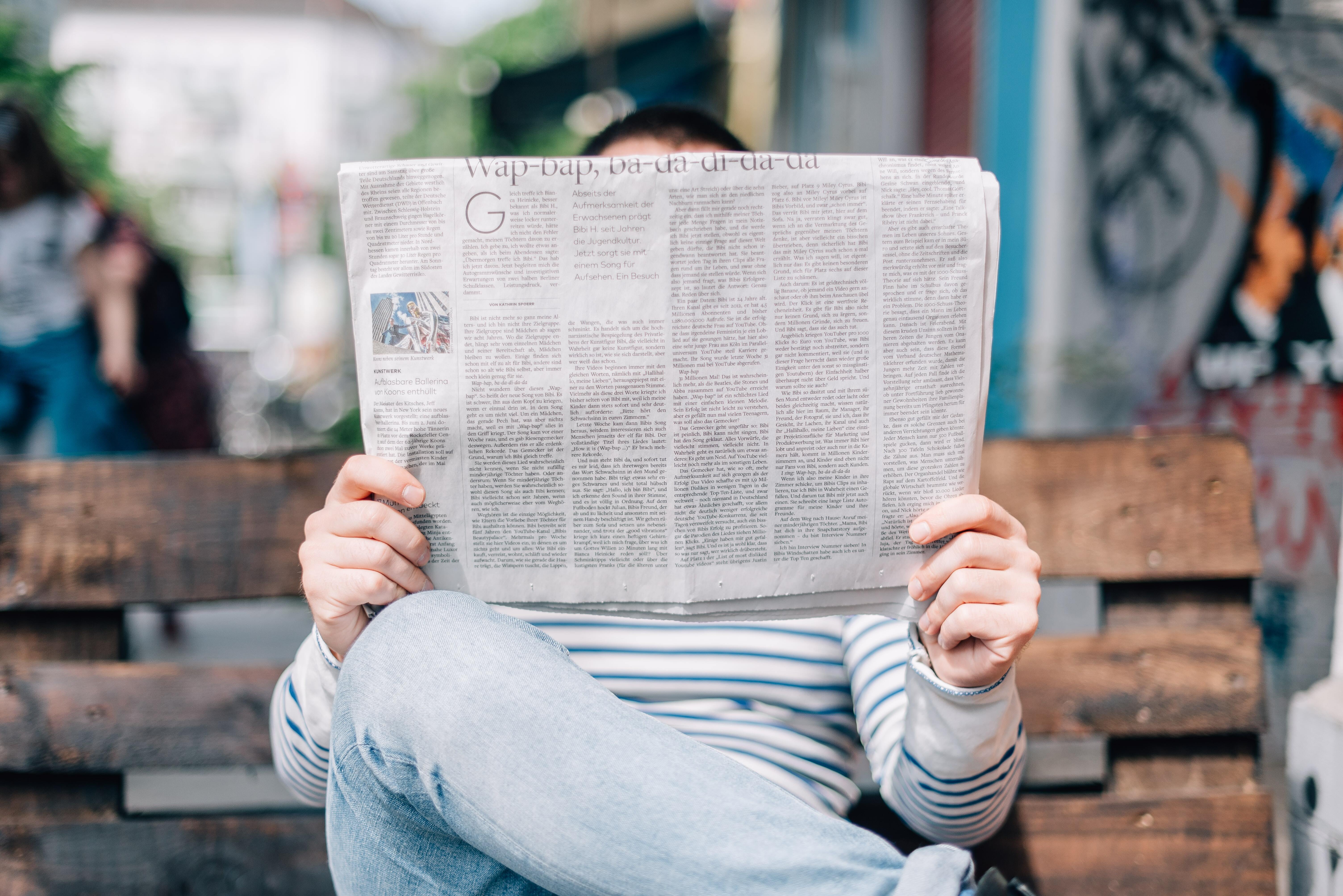 Person reading a newspaper, their face is obscured by the paper.