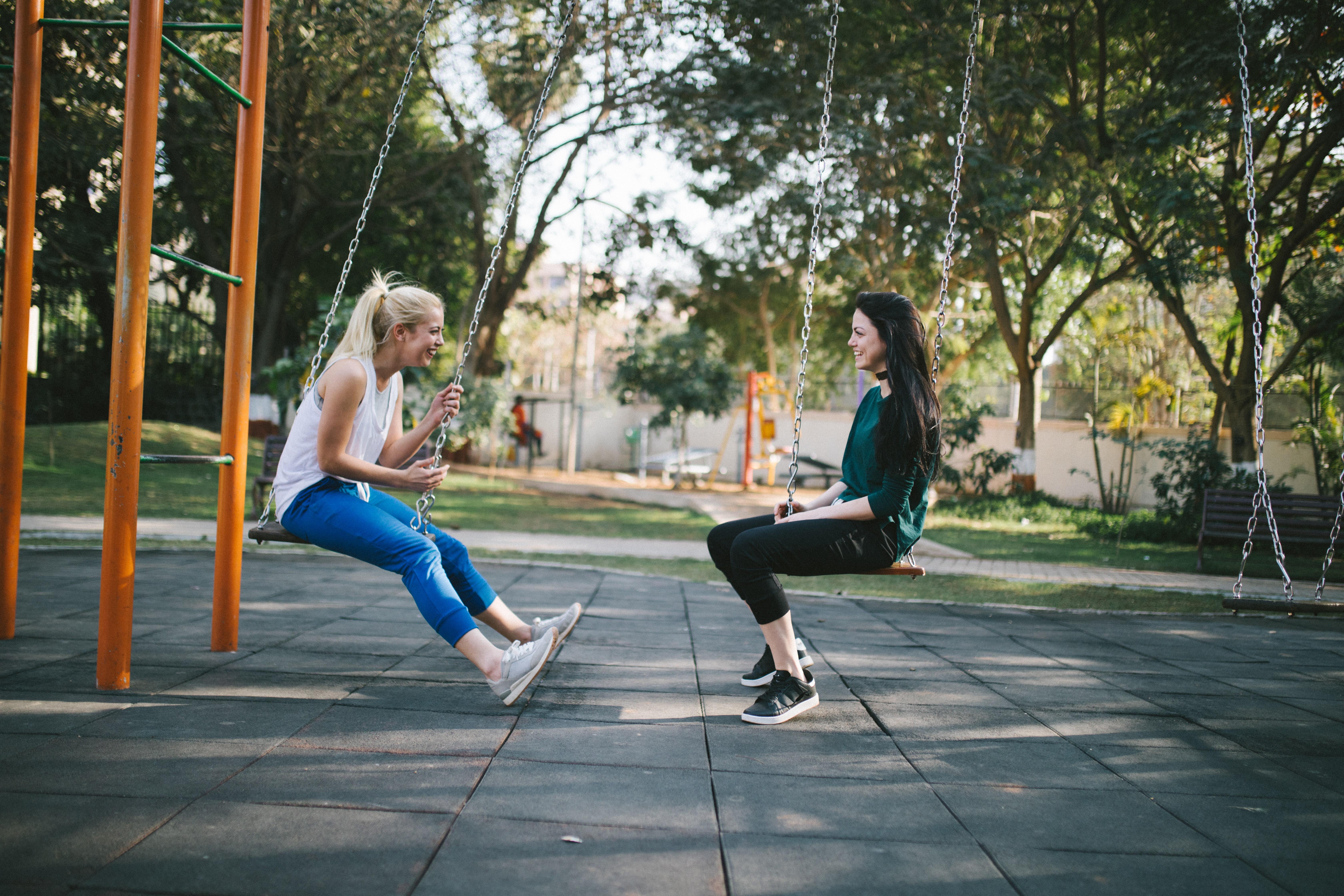 Two girls sitting on swings in a playground