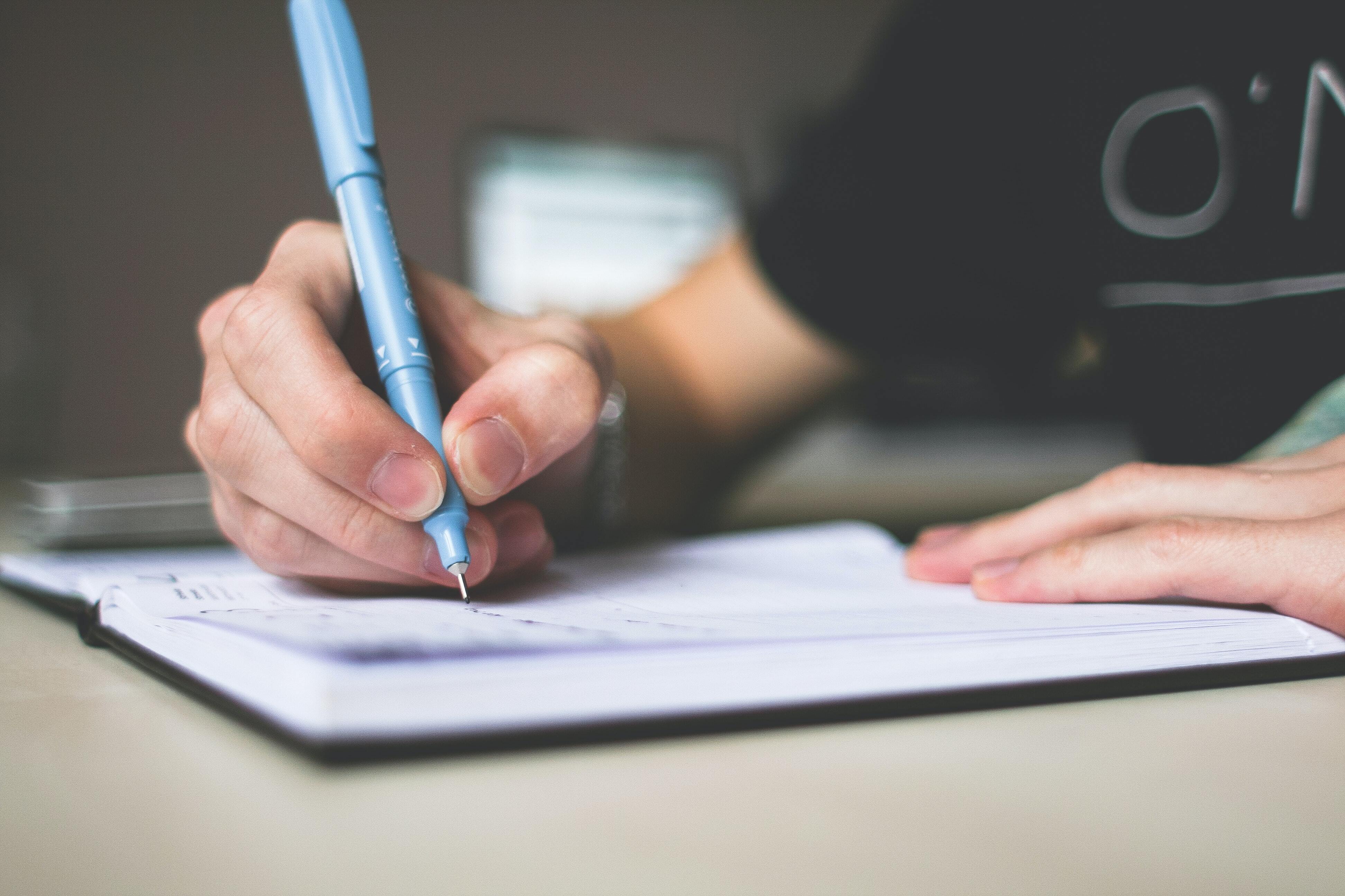 person holding a blue ball point pen to paper