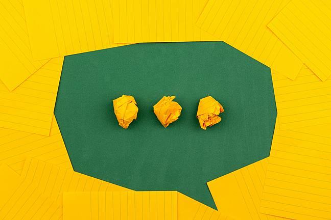 orange sheets of paper lie on a green school board and form a chat bubble with three crumpled papers.