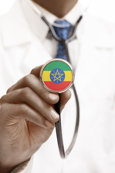 A male doctor holds a stethoscope up to the camera. The tip of the stethoscope is covered in the colours of the Ethiopian flag