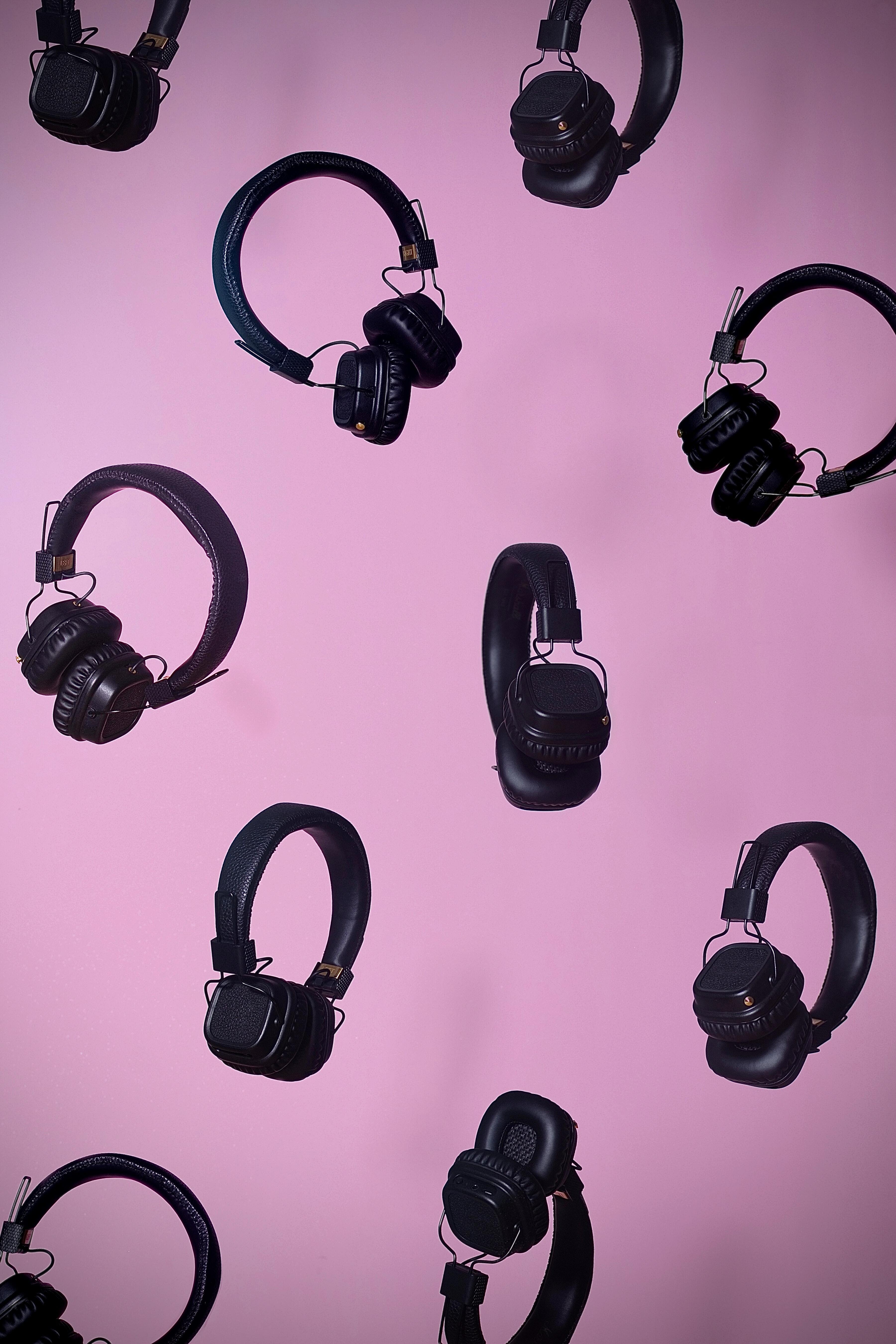 Lots of black over-ear headphones on a pink background.