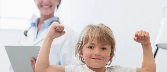 Image of smiling child showing biceps and doctor smiling in the background