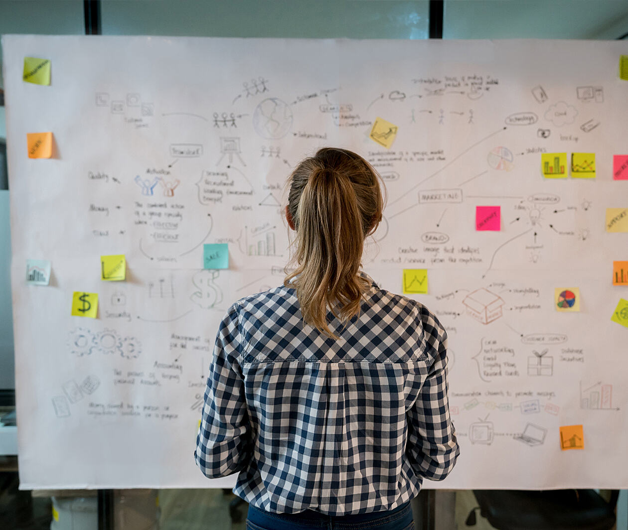 Someone standing in front of a large white screen with lots of notes and post-its on it.