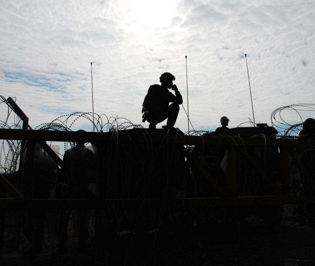 Israeli soldiers guarding a barrier, silhouetted against afternoon sun. 