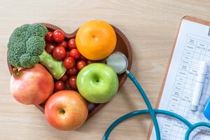 Heart-shaped wooden bowl full of fruit. Sitting on a wooden table next to a stethoscope. 