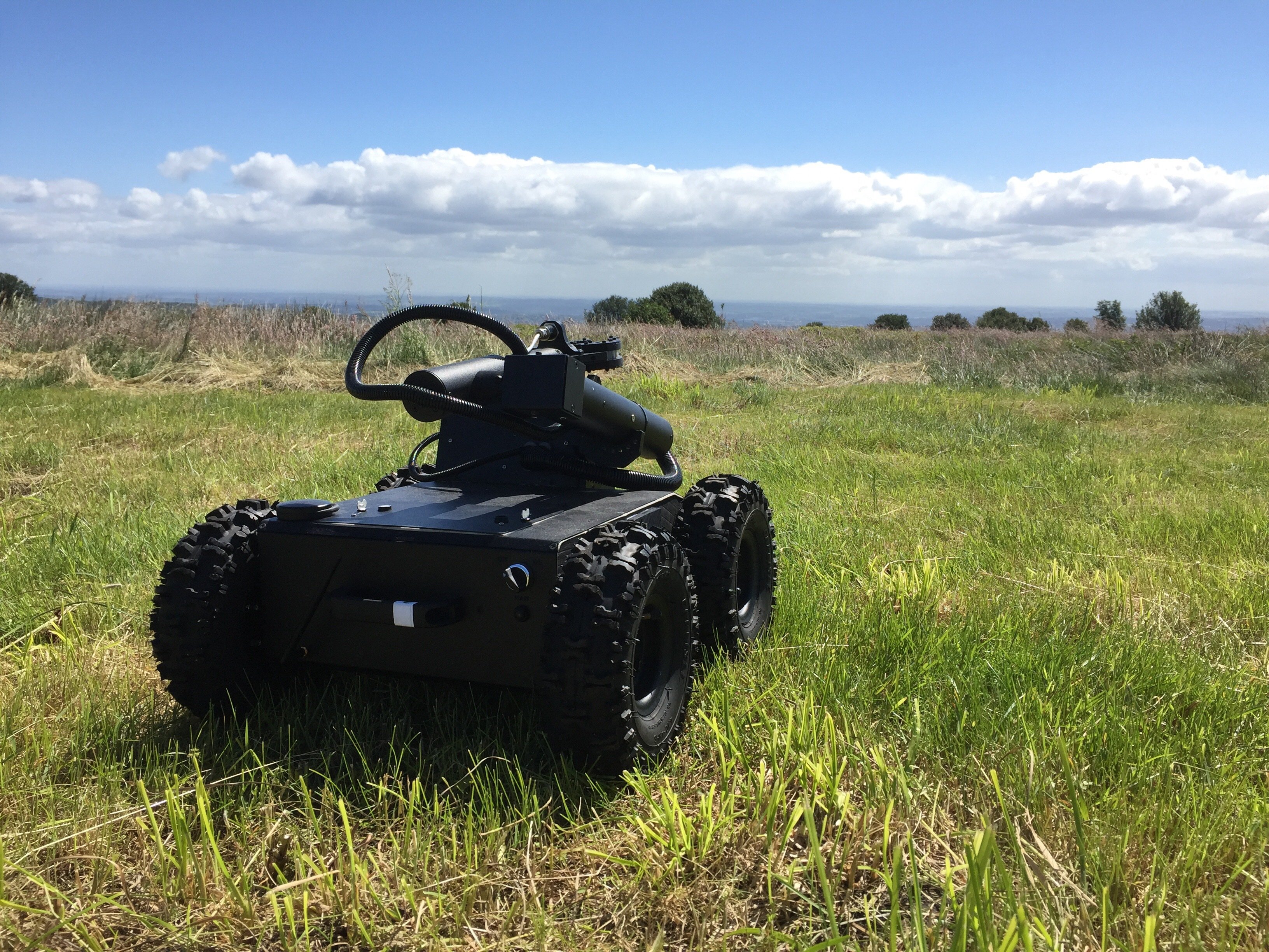 A four-wheeled robot vehicle with off-road tyres looks out across our Field Robotics site